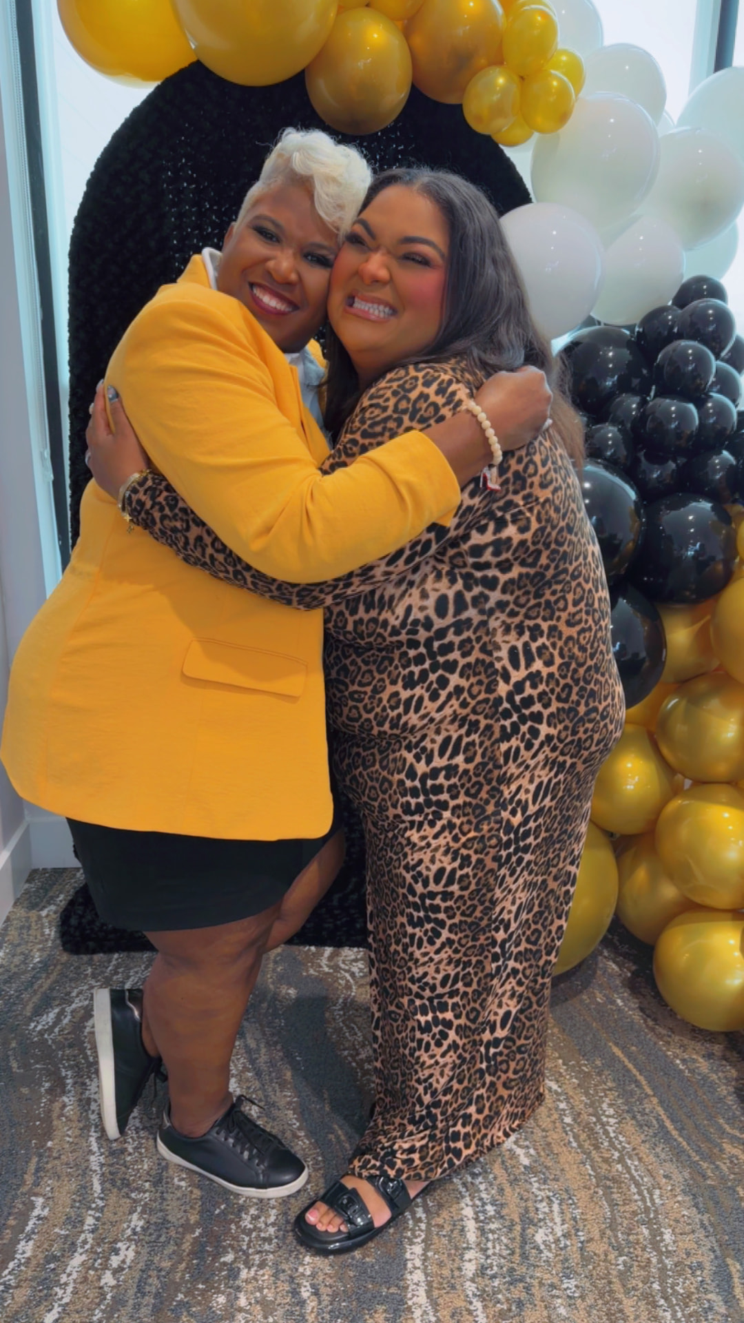 Toya and a member in a leopard-print dress hugging beside the balloon arch