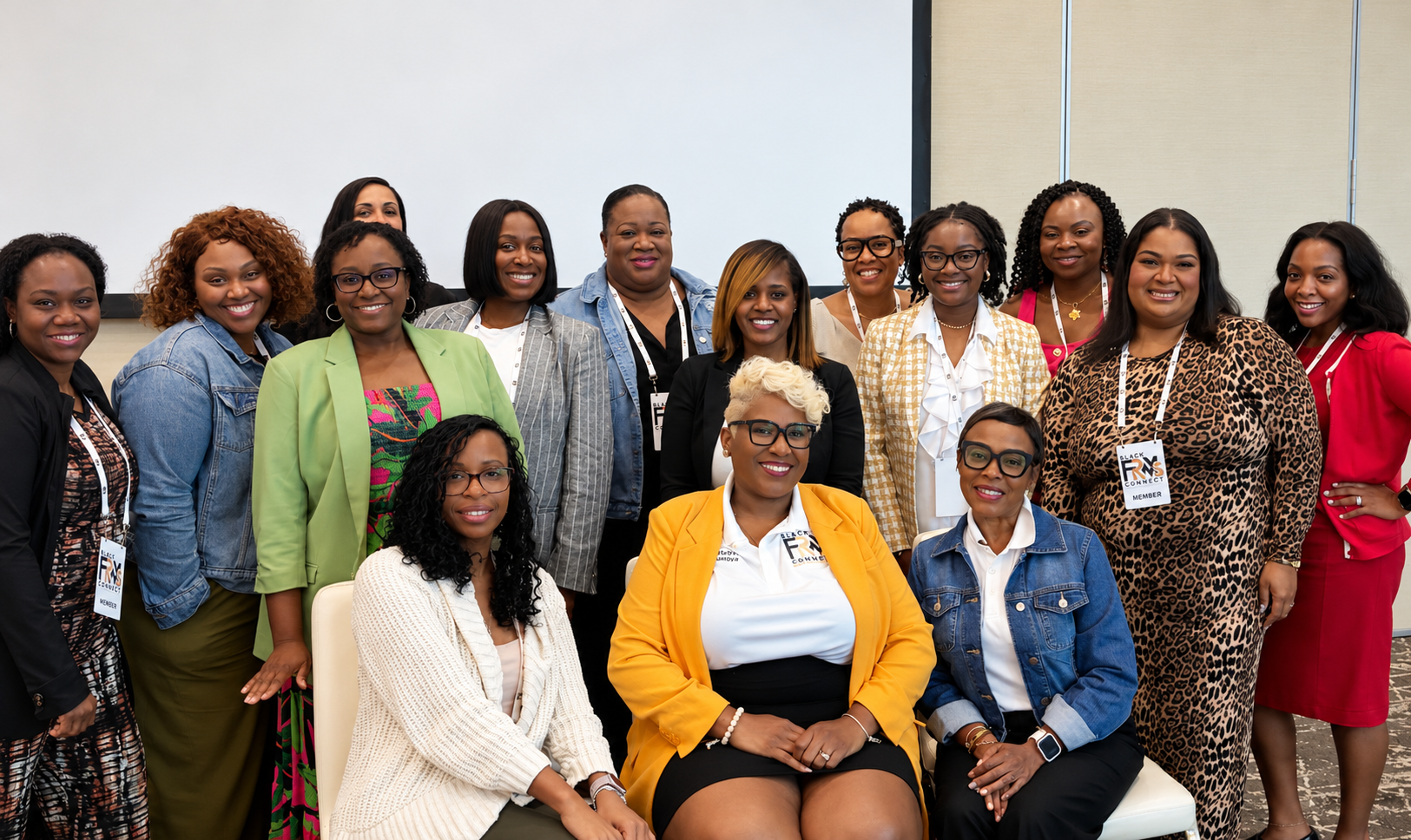 Black FRMs Connect members in professional attire, wearing member lanyards and badges, smiling together in front of a projection screen at the close of a conference session