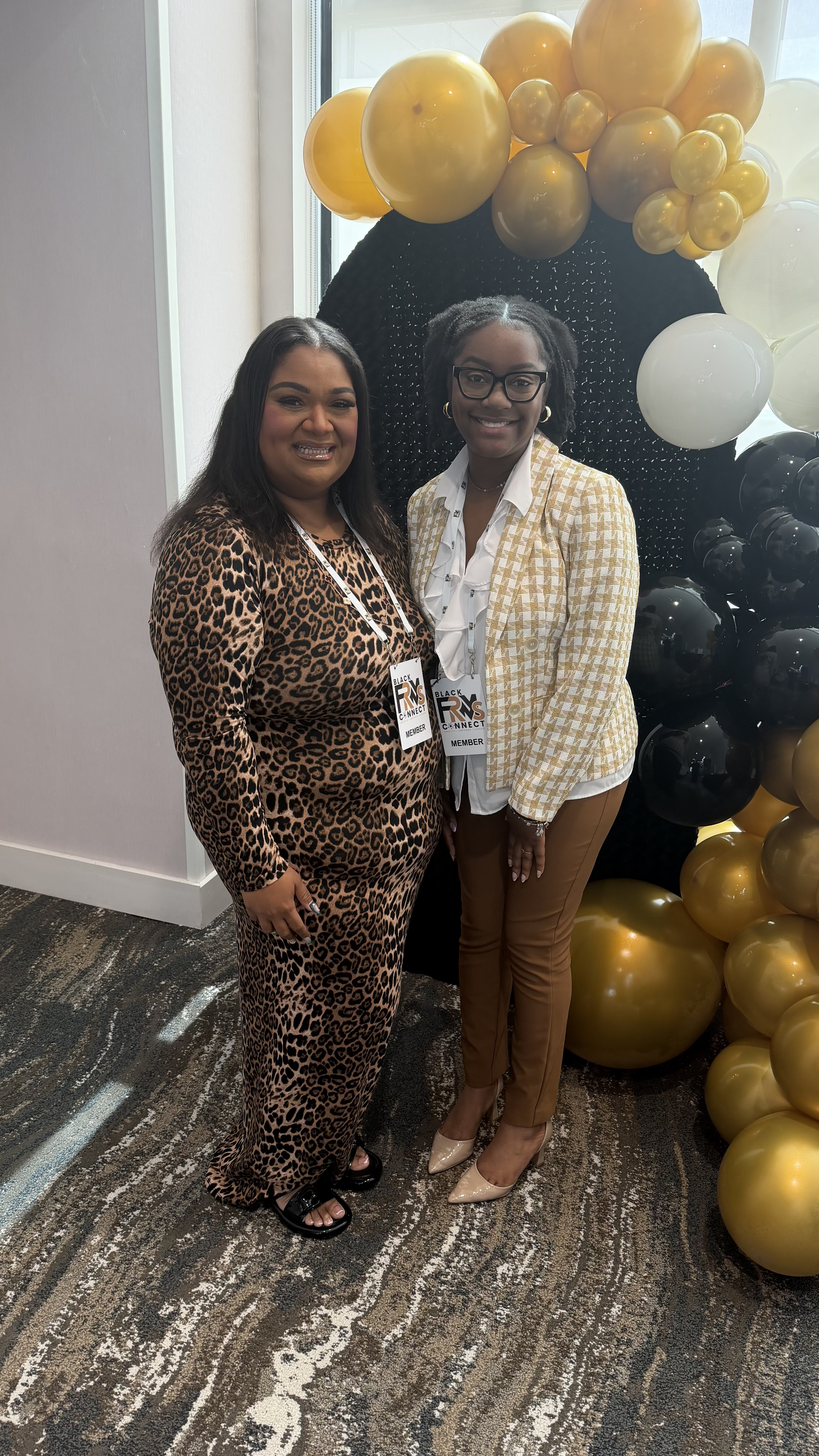 Two members wearing Black FRMs Connect badges smiling at the balloon arch
