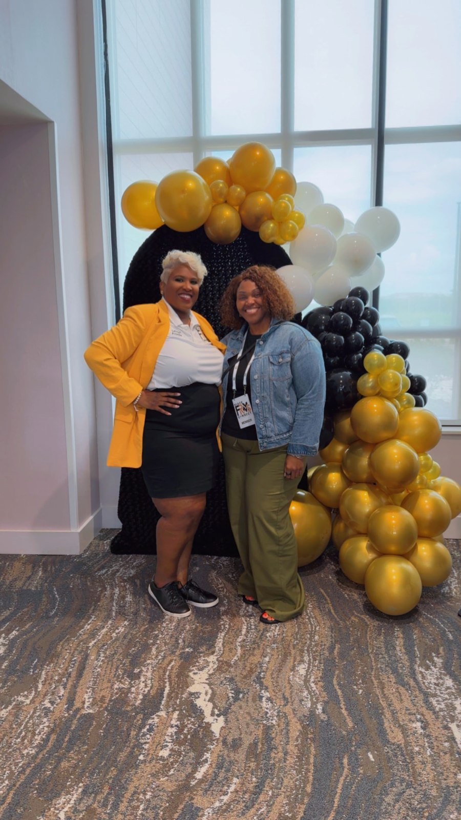 Toya in a gold blazer beside a member in a denim jacket at the balloon arch
