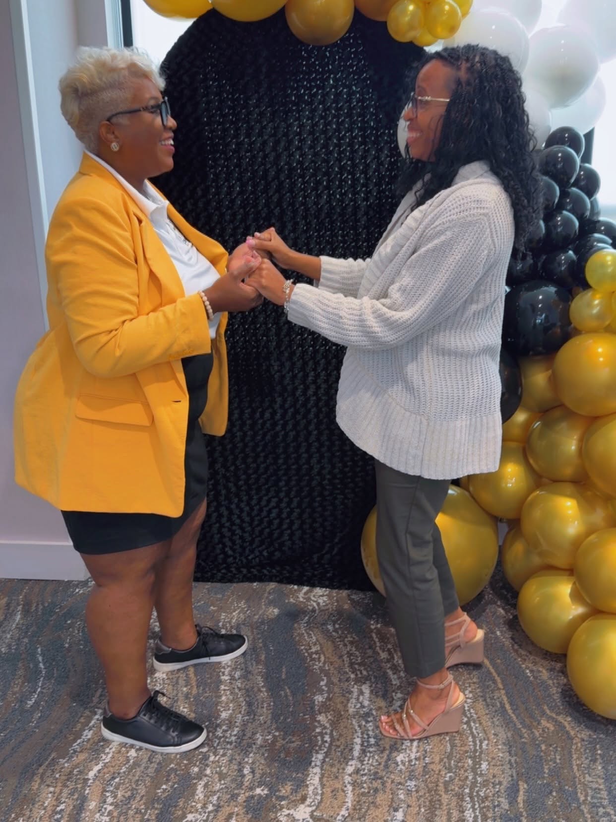 Founder Latoya Wise greeting a community member with joined hands in front of the community's balloon arch